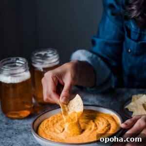 dipping tortilla chip into a bowl of cheesy buffalo cauliflower dip