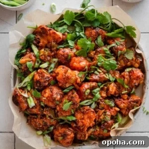 Gobi Manchurian in a parchment paper lined plate with scallions and cilantro as garnish, on white tile surface