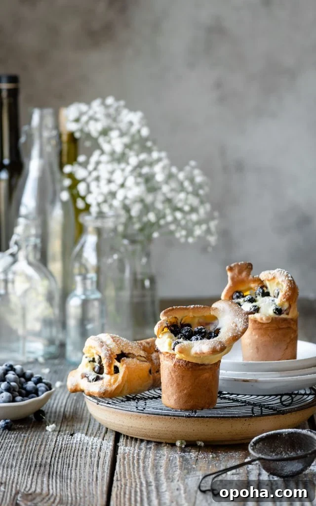 Fluffy Blueberry Popovers: Light, Crispy Breakfast Treat 5 Blueberry popovers on table with bowl of fresh blueberries.
