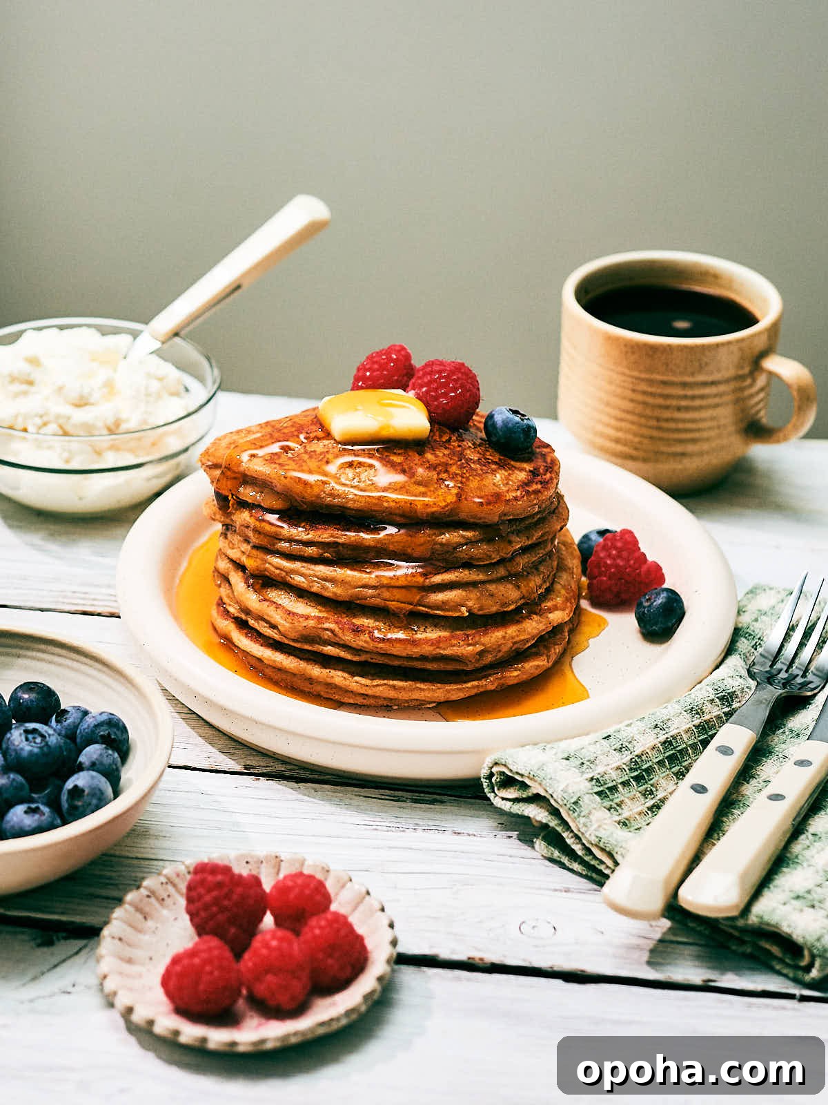 High-Protein Cottage Cheese Pancakes for Muscle Gain and Weight Loss 11 A stack of high protein Cottage Cheese pancakes on a plate with berries, maple syrup and butter.