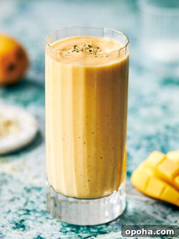 Mango protein smoothie in a glass with hemp seeds sprinkled on top.