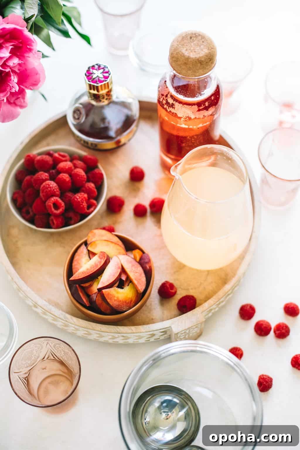 Fresh raspberries, fresh peach slices, lemonade in a pitcher, rosè in a pitcher and chambord on a wooden serving platter.