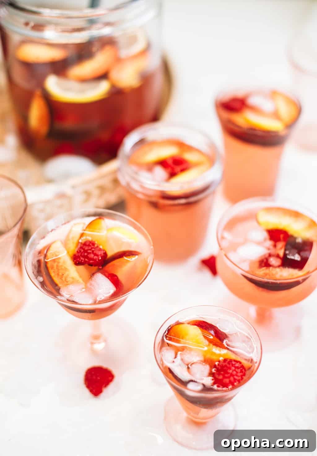 Rosè sangria with peaches and raspberries served in pink wine glasses. 