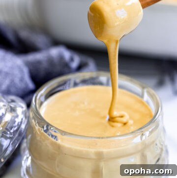 A wooden honey dipper is pouring whipped honey into a glass honey jar
