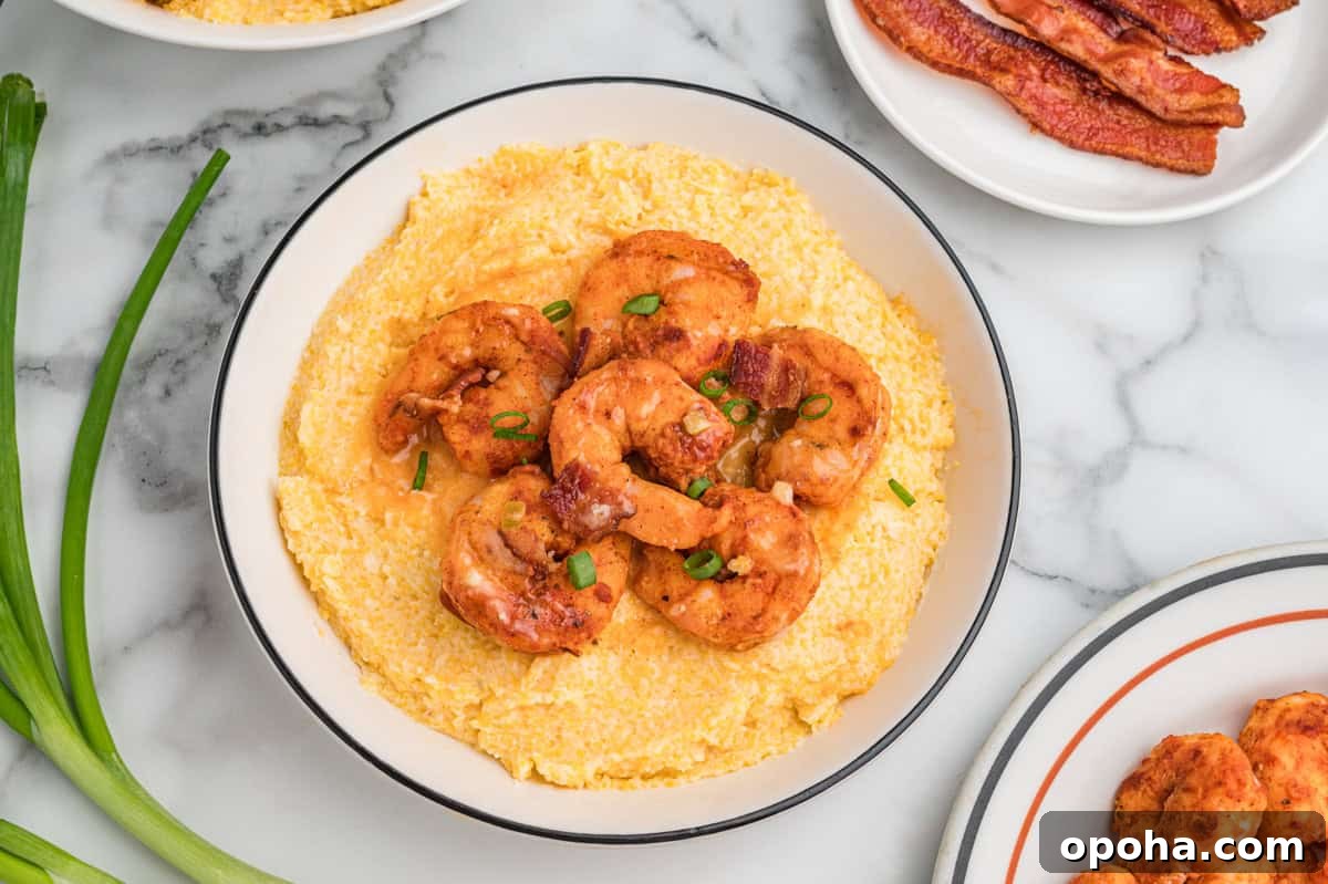 Creamy Shrimp and Grits with Cheddar and Garlic 11 Bowl of cheesy grits topped with shrimp, bacon pieces, and scallions. The bowl is surrounded by fresh green onions and a plate of bacon.
