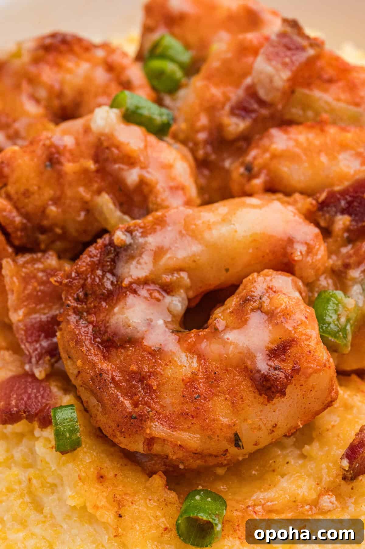 Creamy Shrimp and Grits with Cheddar and Garlic 3 Saucy, seasoned shrimp resting on creamy yellow grits, with visible pieces of green onion and bacon.