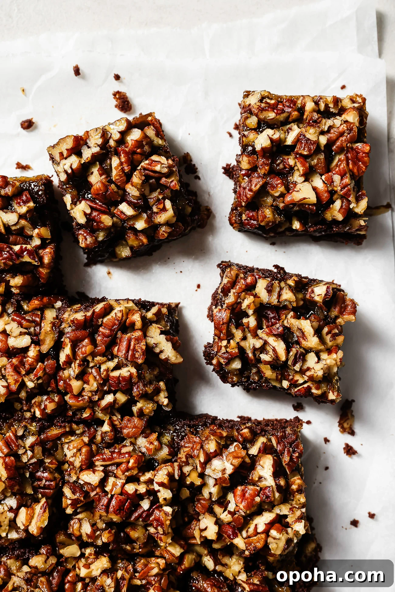 Overhead view of pecan pie brownies cut into squares on parchment paper, featuring a gooey chocolate base and caramelized pecan topping.
