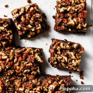 Overhead view of pecan pie brownies cut into squares on parchment paper, featuring a gooey chocolate base and caramelized pecan topping.