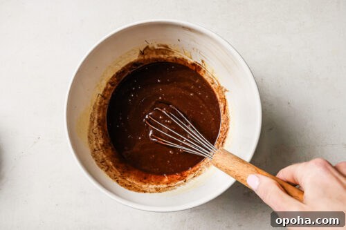 Rich pecan pie brownie batter in a white mixing bowl, ready to be poured into the pan for baking.
