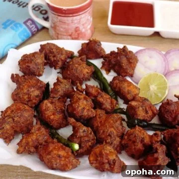 fried chicken pakora on a white plate. Served with fried green chilies and lemon.