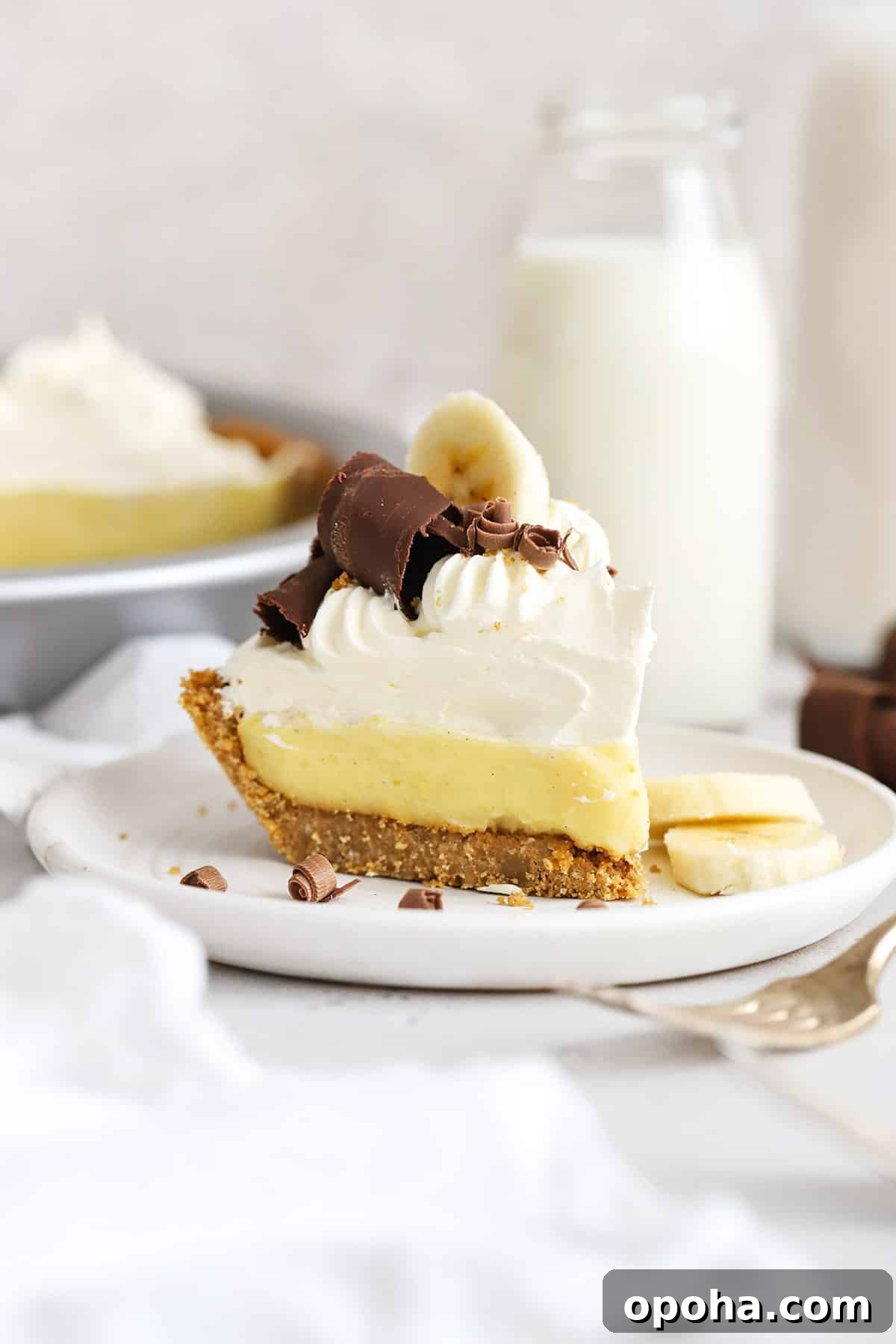 Gluten-Free Banana Cream Pie Recipe — Light, Silky & Delicious 8 Front view of a slice of gluten-free banana cream pie topped with whipped cream and chocolate curls