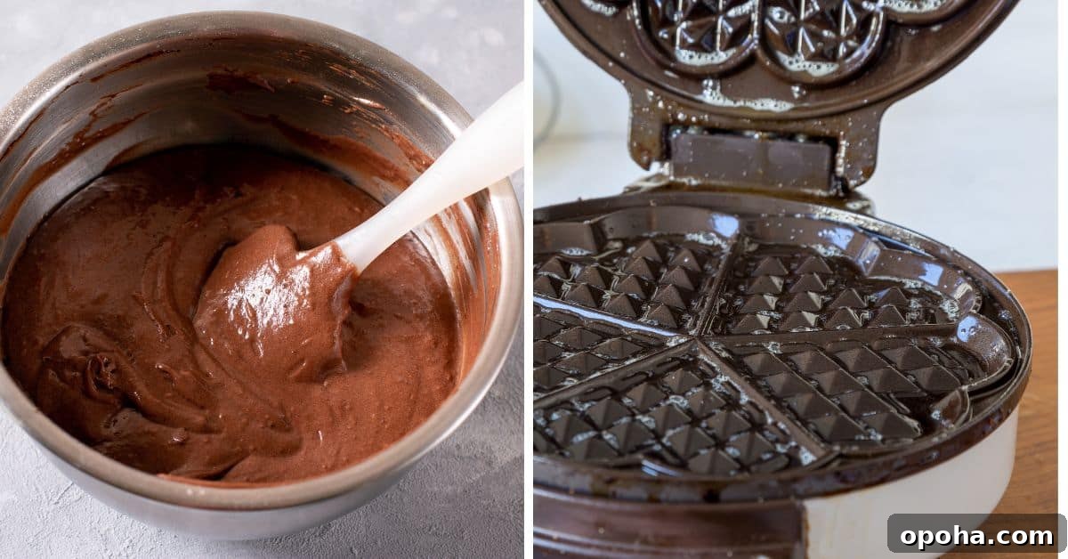 A bowl of chocolate batter, perfect for making Chocolate Waffles, sits with a spatula beside an open, greased waffle iron.
