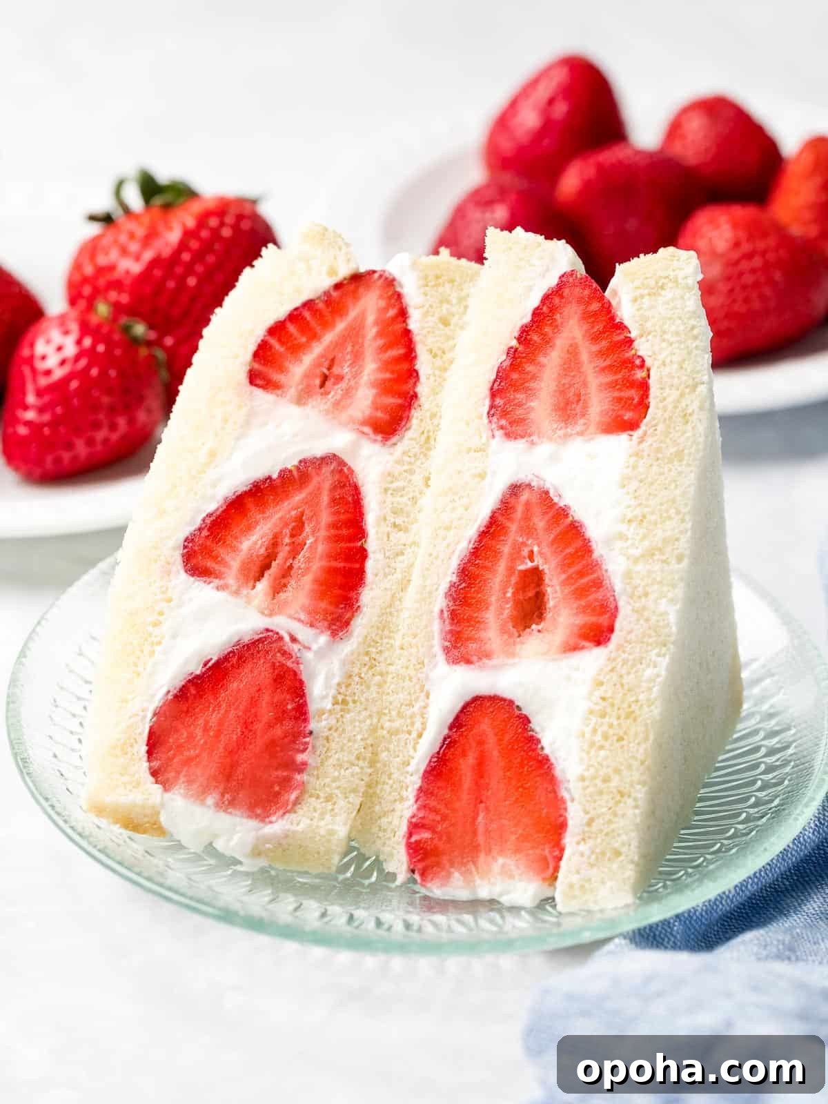 Japanese Fruit Sandwich (Strawberry Sando): How to Make フルーツサンド 2 Japanese fruit sando made with strawberries and whipped cream sliced in half next to a plate of red strawberries.