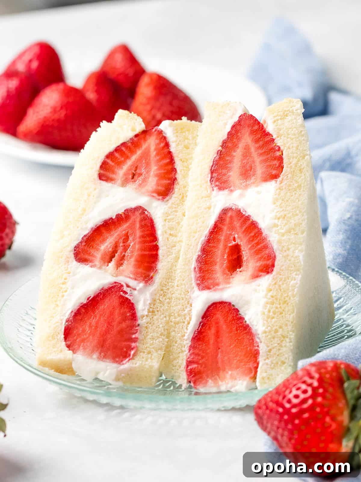 Japanese Fruit Sandwich (Strawberry Sando): How to Make フルーツサンド 15 Japanese strawberry sando made with red strawberries and whipped cream sliced in half next to a plate of strawberries.