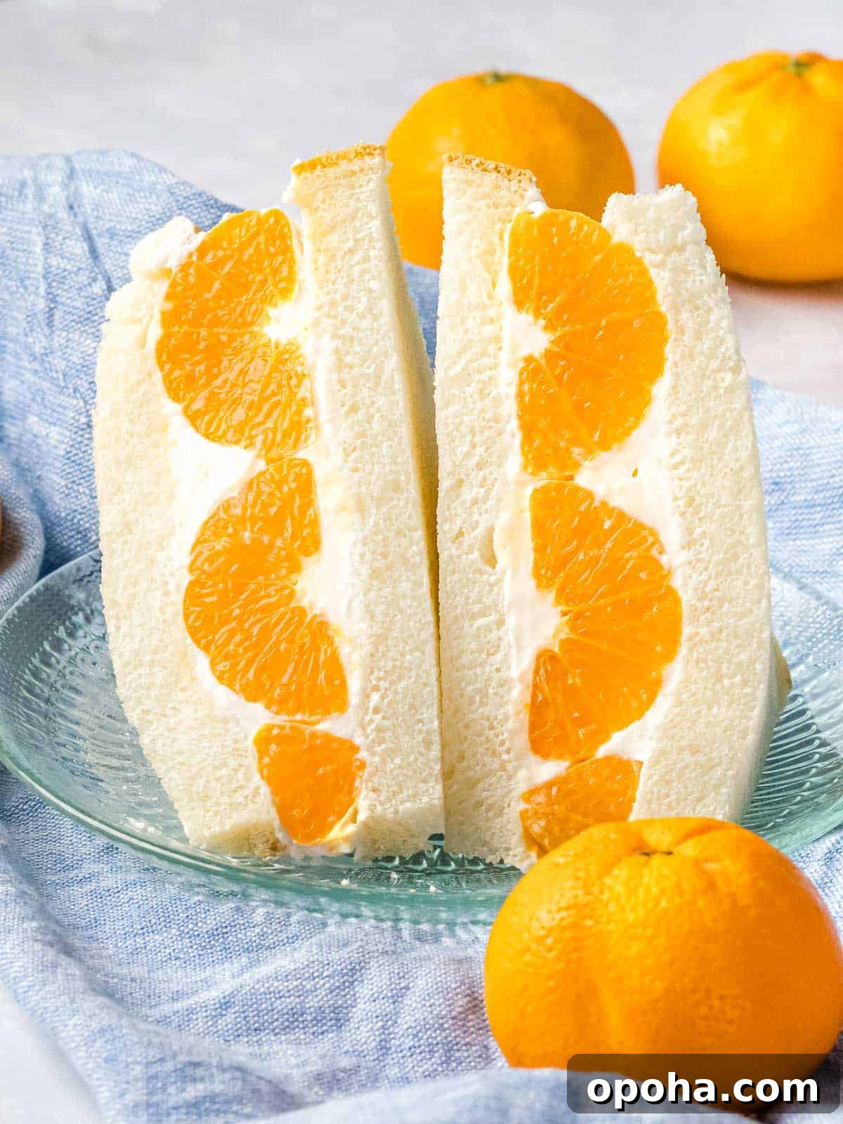 Japanese Fruit Sandwich (Strawberry Sando): How to Make フルーツサンド 16 Japanese fruit sando made with mandarin oranges that's sliced in half on a glass plate.
