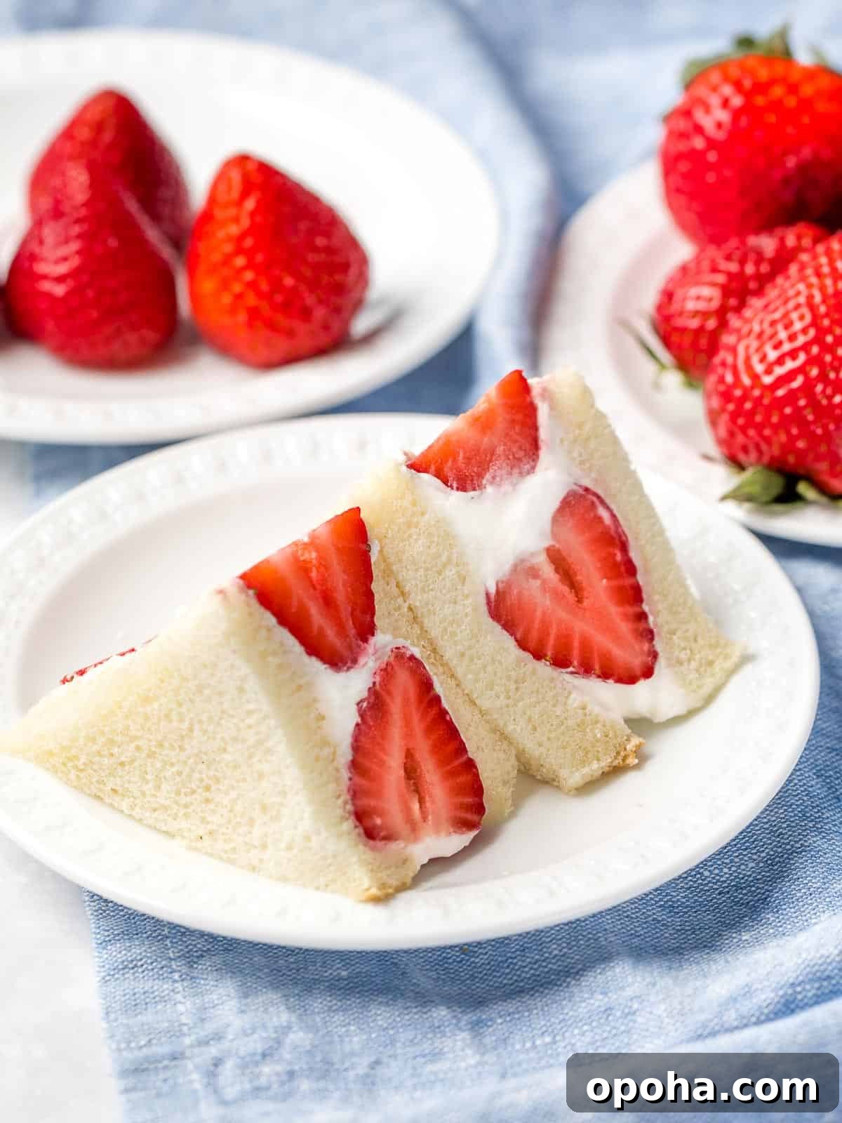 Japanese Fruit Sandwich (Strawberry Sando): How to Make フルーツサンド 3 Japanese strawberry sando cut into quarters on a white plate next to red strawberries.