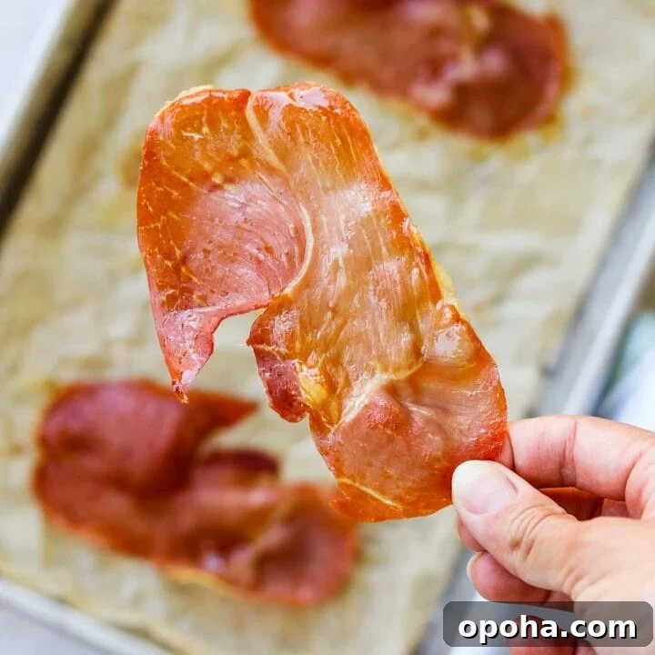 Hand holding a piece of oven-roasted crispy prosciutto.