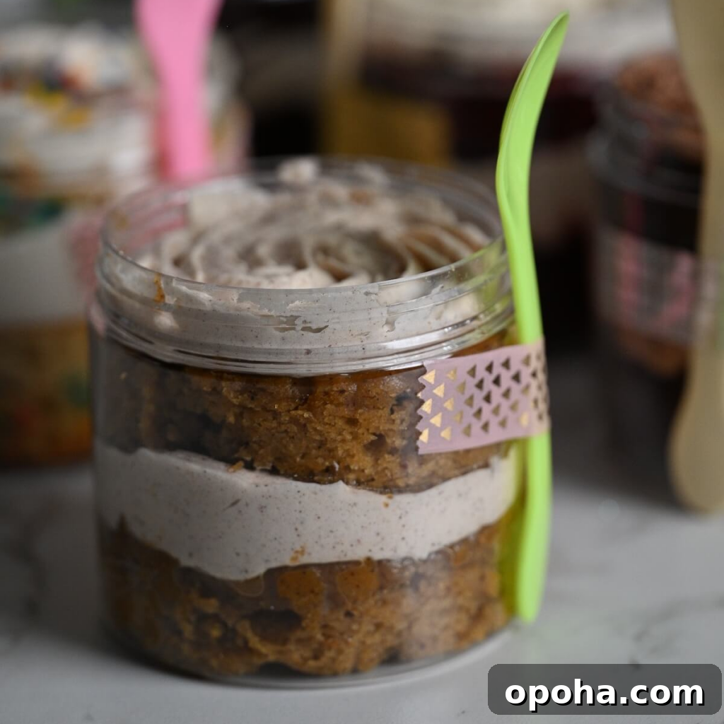 Mason Jar Cake Recipe: Layered Dessert in a Jar 7 close up view of a plastic jar with layers of moist carrot cake and cinnamon buttercream with a spoon and washi tape attached to the jar.