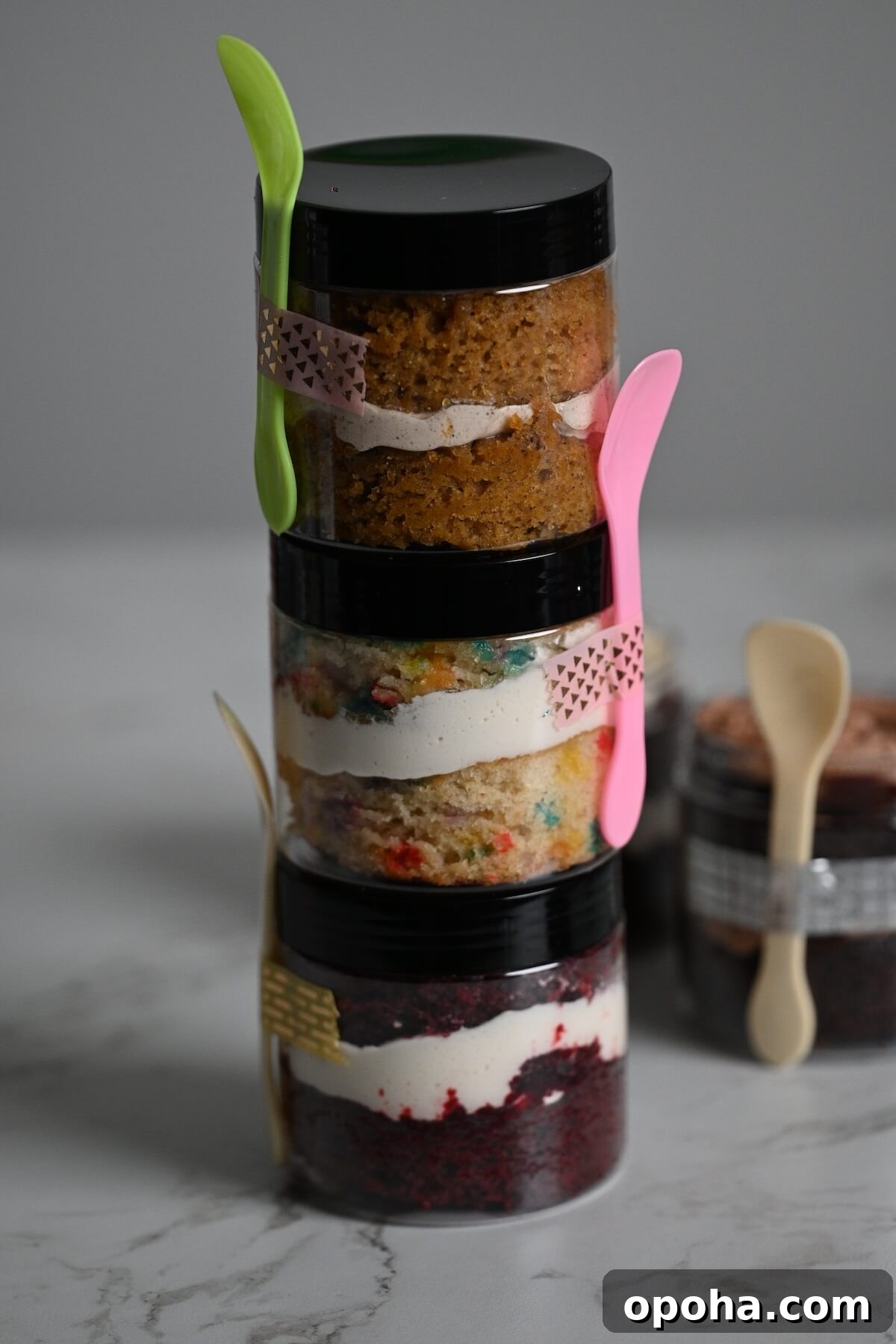 Mason Jar Cake Recipe: Layered Dessert in a Jar 8 tower of stacked cakes in jars with different flavors, like chocolate cake, red velvet cake, funfetti cake, and carrot cake.