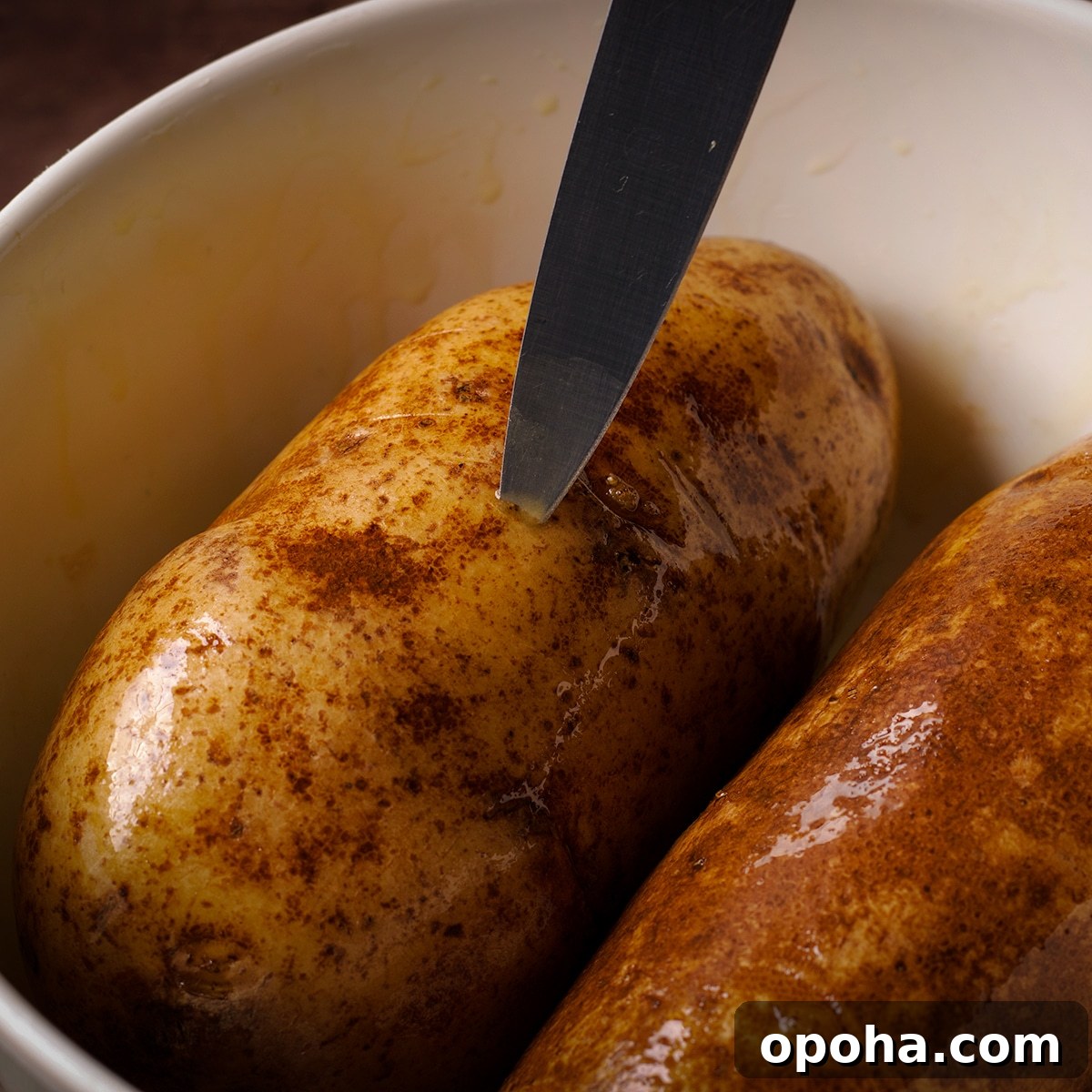 Perfect Crispy Baked Potatoes: Oven-Roasted Recipe and Tips 4 Someone using a knife to poke holes in raw Russet potatoes.