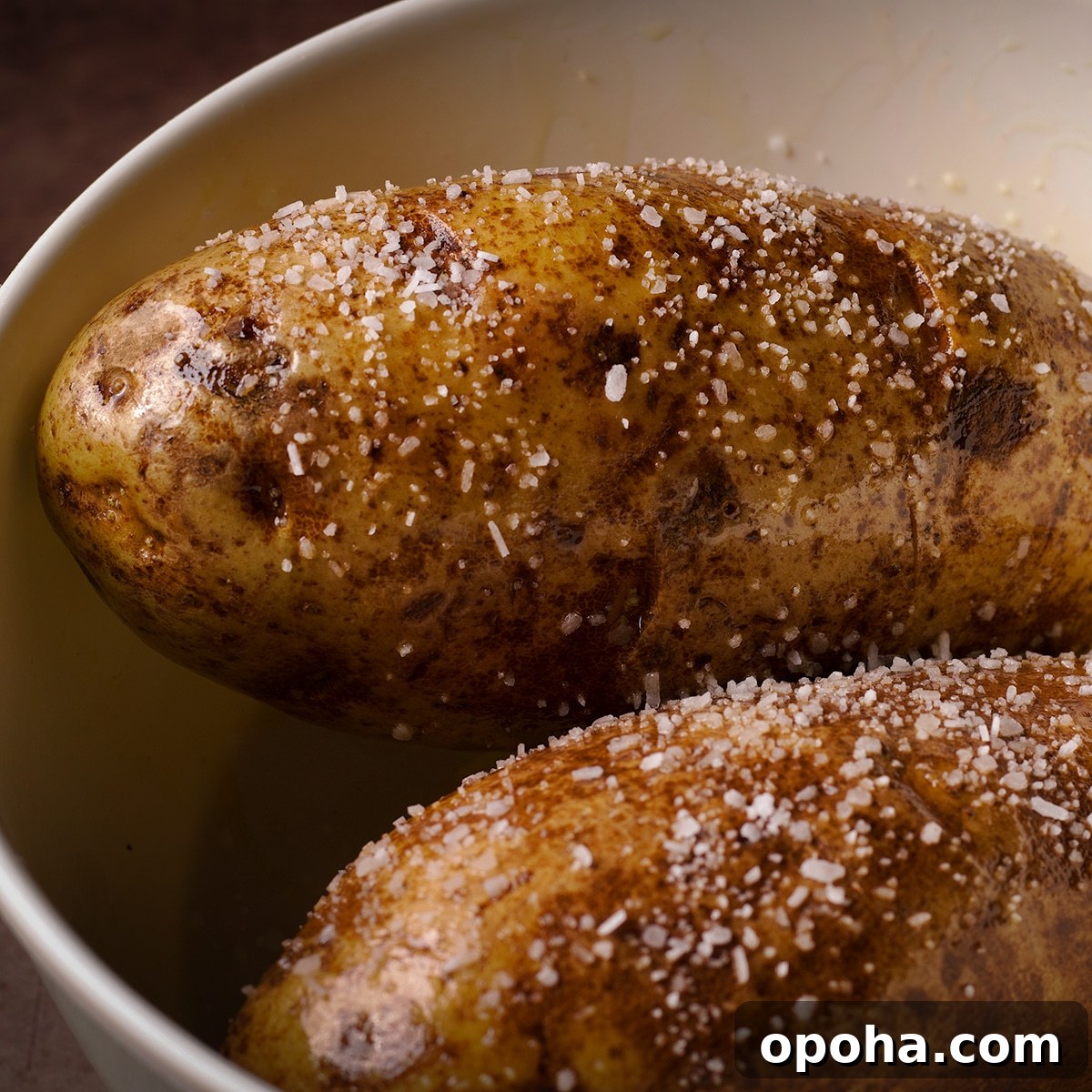 Perfect Crispy Baked Potatoes: Oven-Roasted Recipe and Tips 5 Two Russet potatoes in a bowl covered with olive oil and salt.