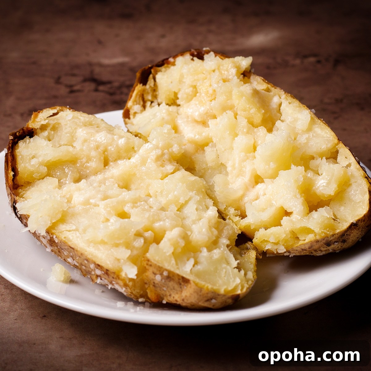 Perfect Crispy Baked Potatoes: Oven-Roasted Recipe and Tips 8 A hot baked potato on a white plate, split in half and ready to eat.