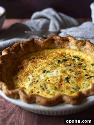 Angled view of tomato, leek and feta quiche on a brown surface with tomatoes and a linen in the background