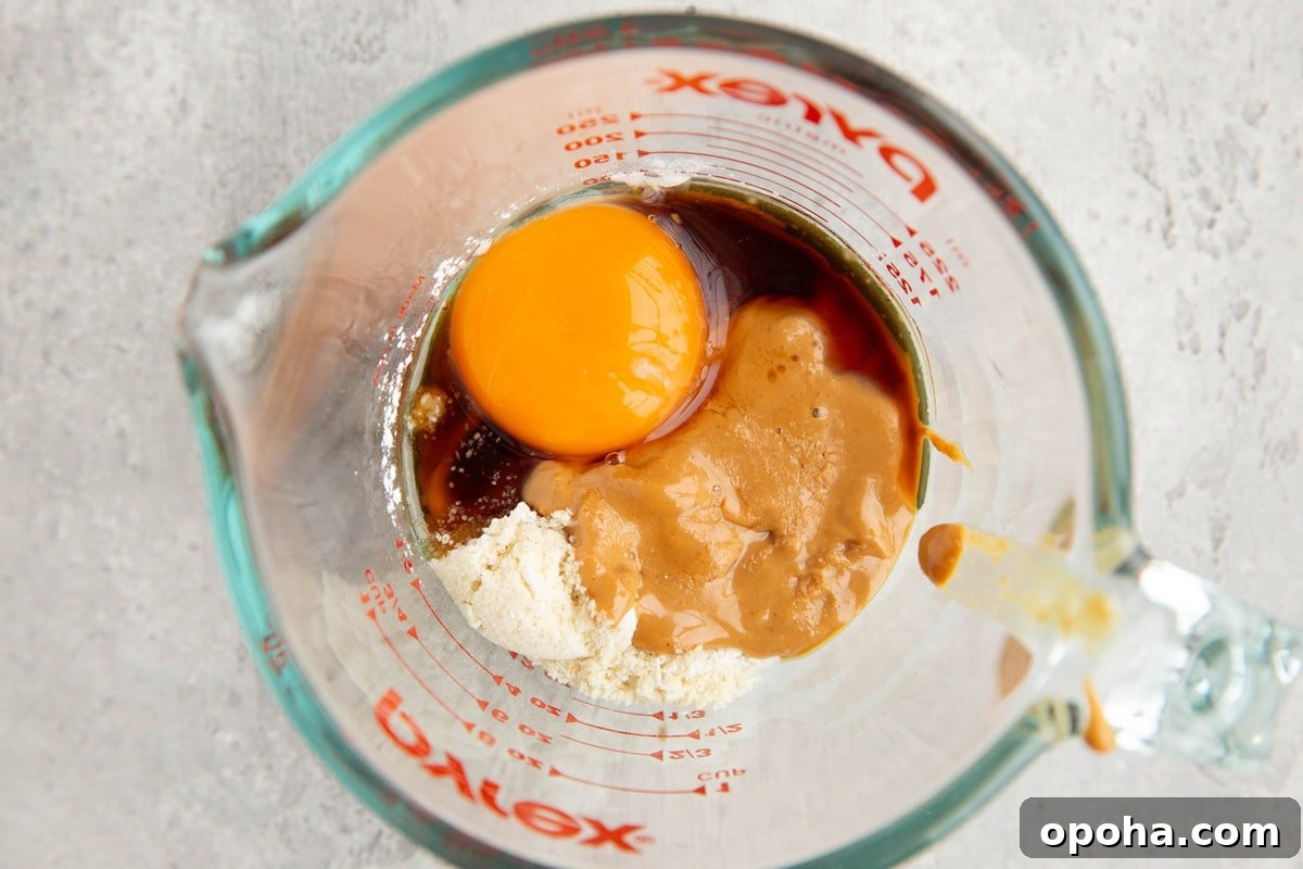 Measuring cup full of ingredients for an almond flour peanut butter mug cake.