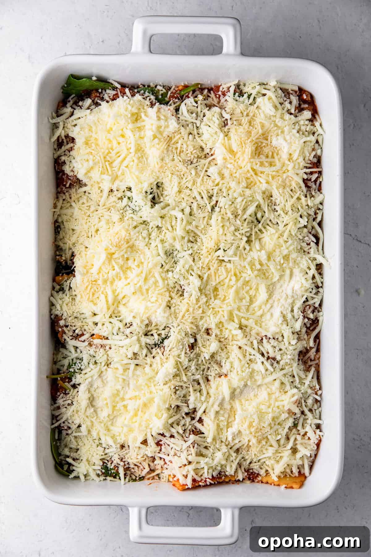 casserole dish with ravioli mixture, ricotta and shredded cheeses