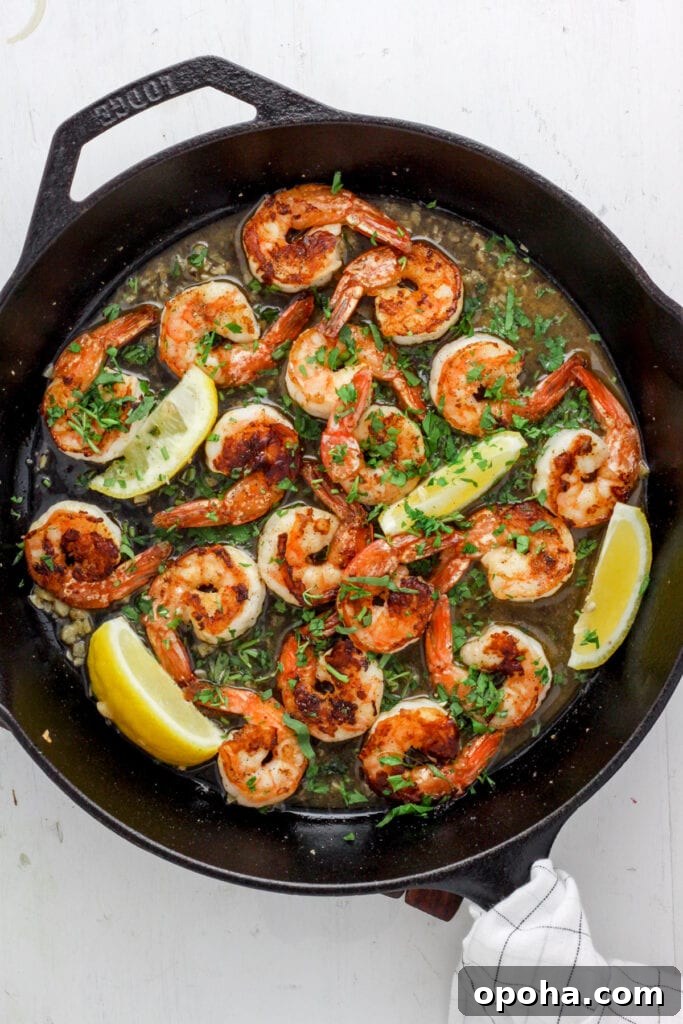 Skillet with seared shrimp, white wine sauce, herbs and lemon wedges.