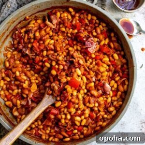 An overhead image of baked beans in a pot with a wooden spoon in the middle.