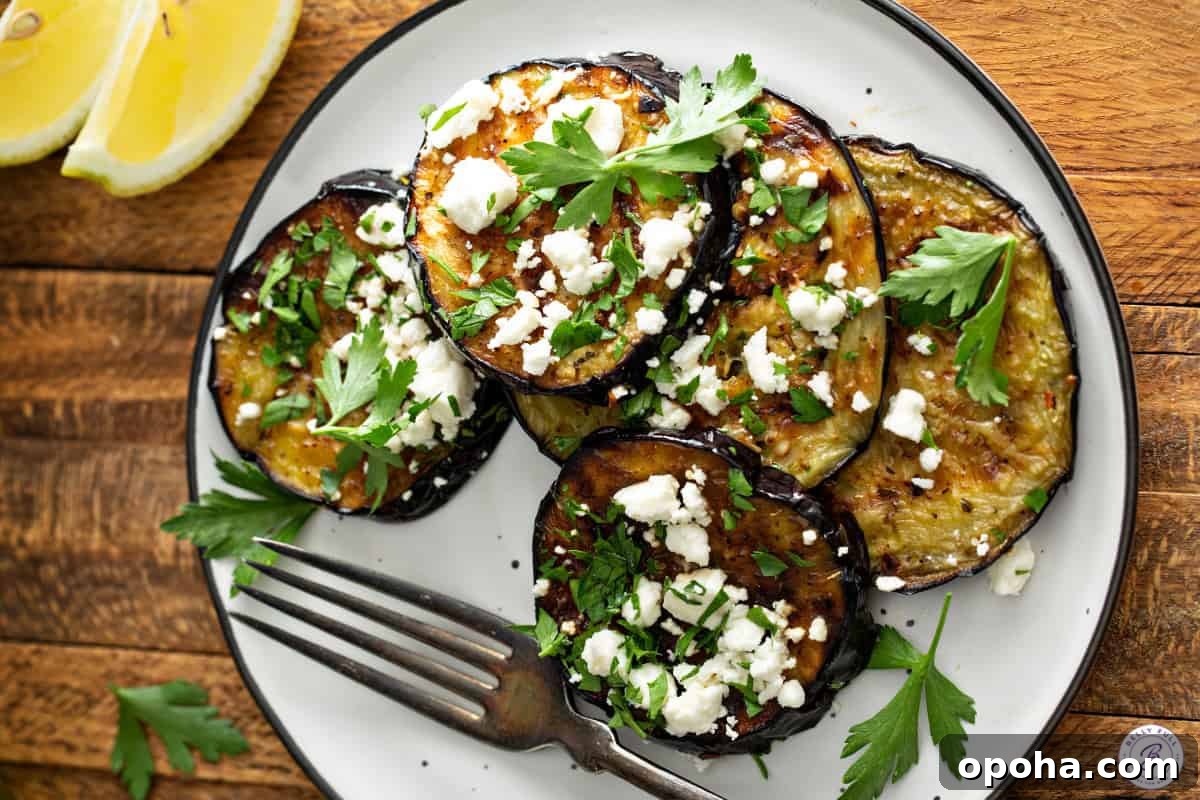Grilled eggplant topped with feta and parsley on a white plate with a fork.