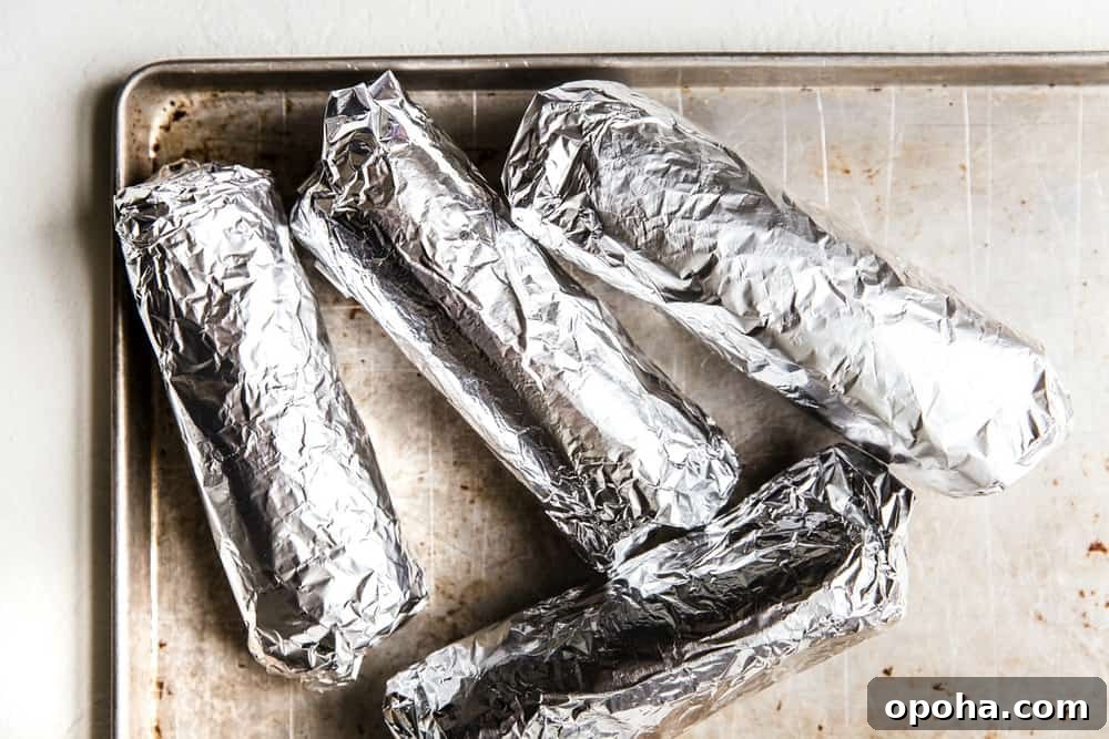 4 Burritos wrapped in aluminum foil on a baking sheet.