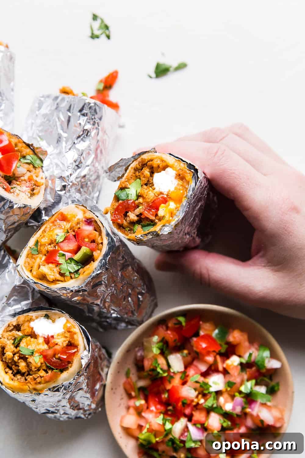 Stack of mini burritos with a brown bowl of salsa on the side.
