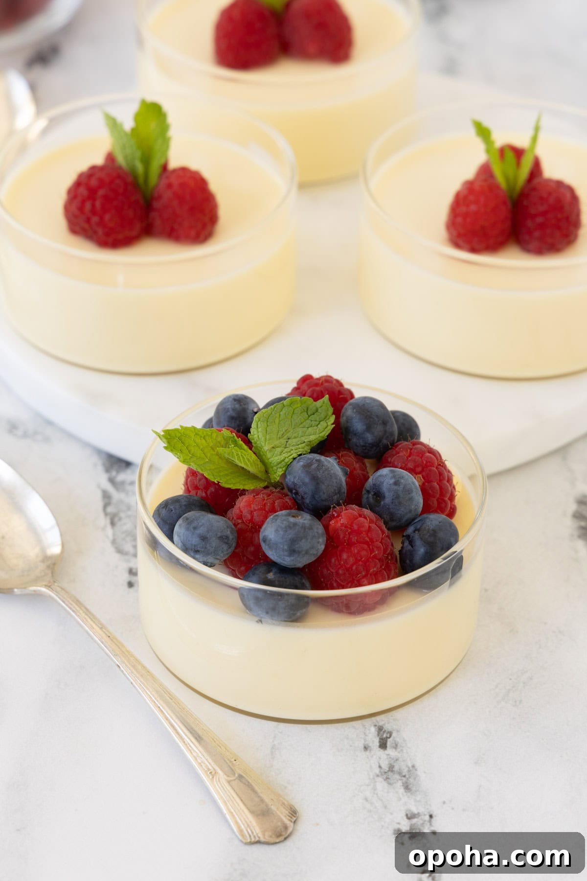 Pale lemon colored lemon possets in glass cups topped with raspberries and blueberries.