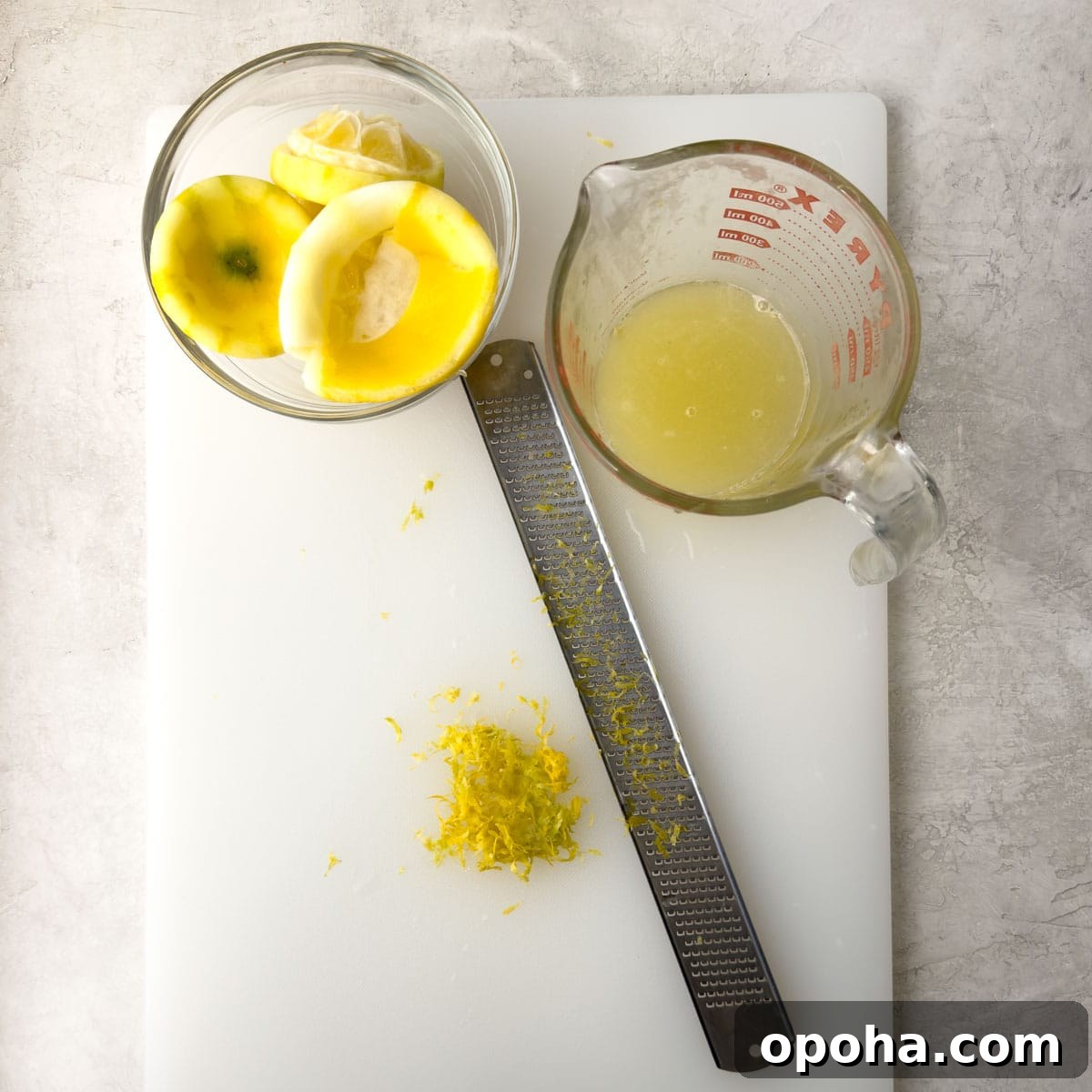 Lemons being juice and zested on a white cutting board with a microplane zester.
