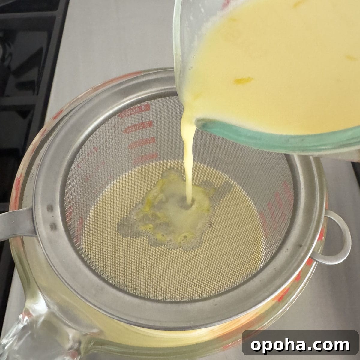 Straining lemon zest through a fine sieve into a large glass measuring cup.