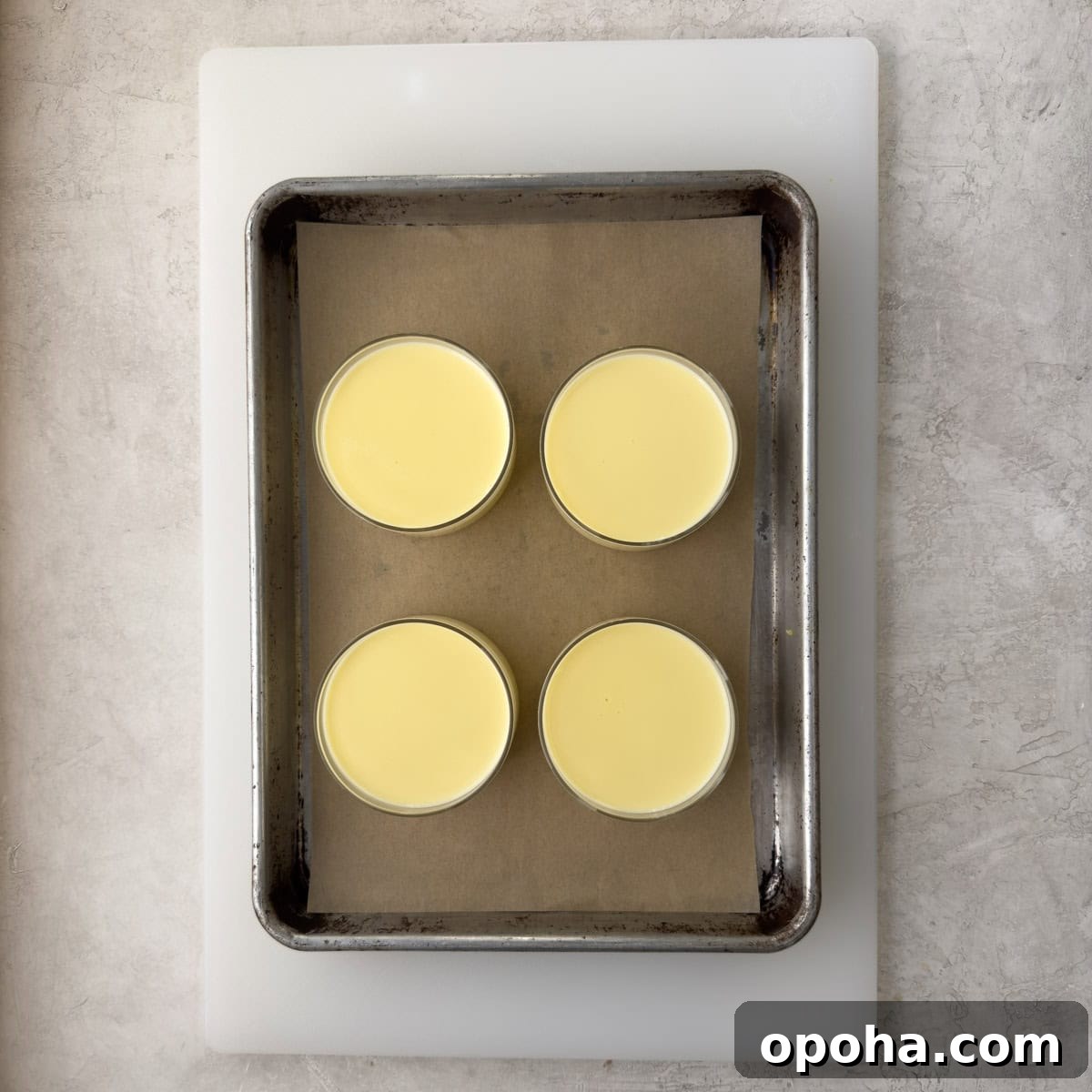Four lemon posset desserts in individual glass cups on a tray and white cutting board.
