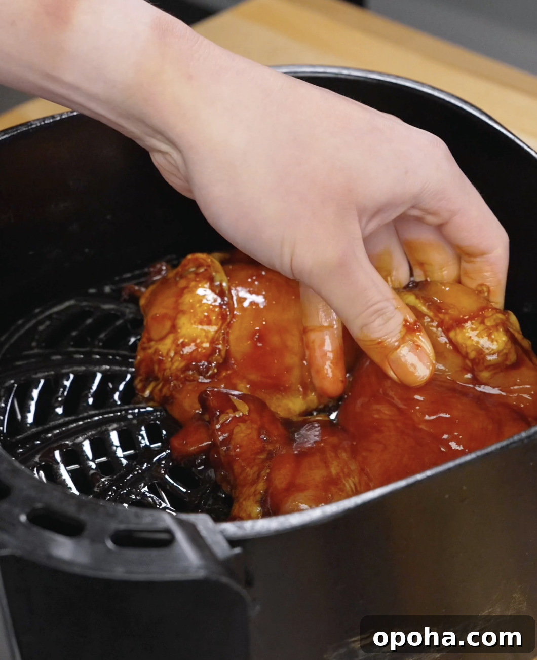 Marinated chicken thighs being placed into an air fryer basket, coated in a rich bulgogi sauce ready to cook until caramelized and juicy.