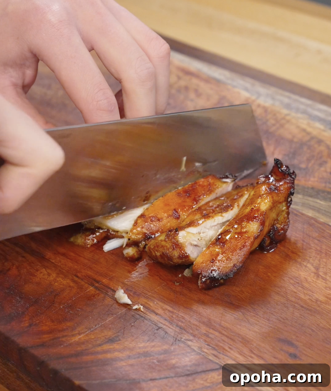 Cooked chicken bulgogi being sliced into thin strips on a wooden cutting board, revealing juicy interior and caramelized exterior from the marinade.
