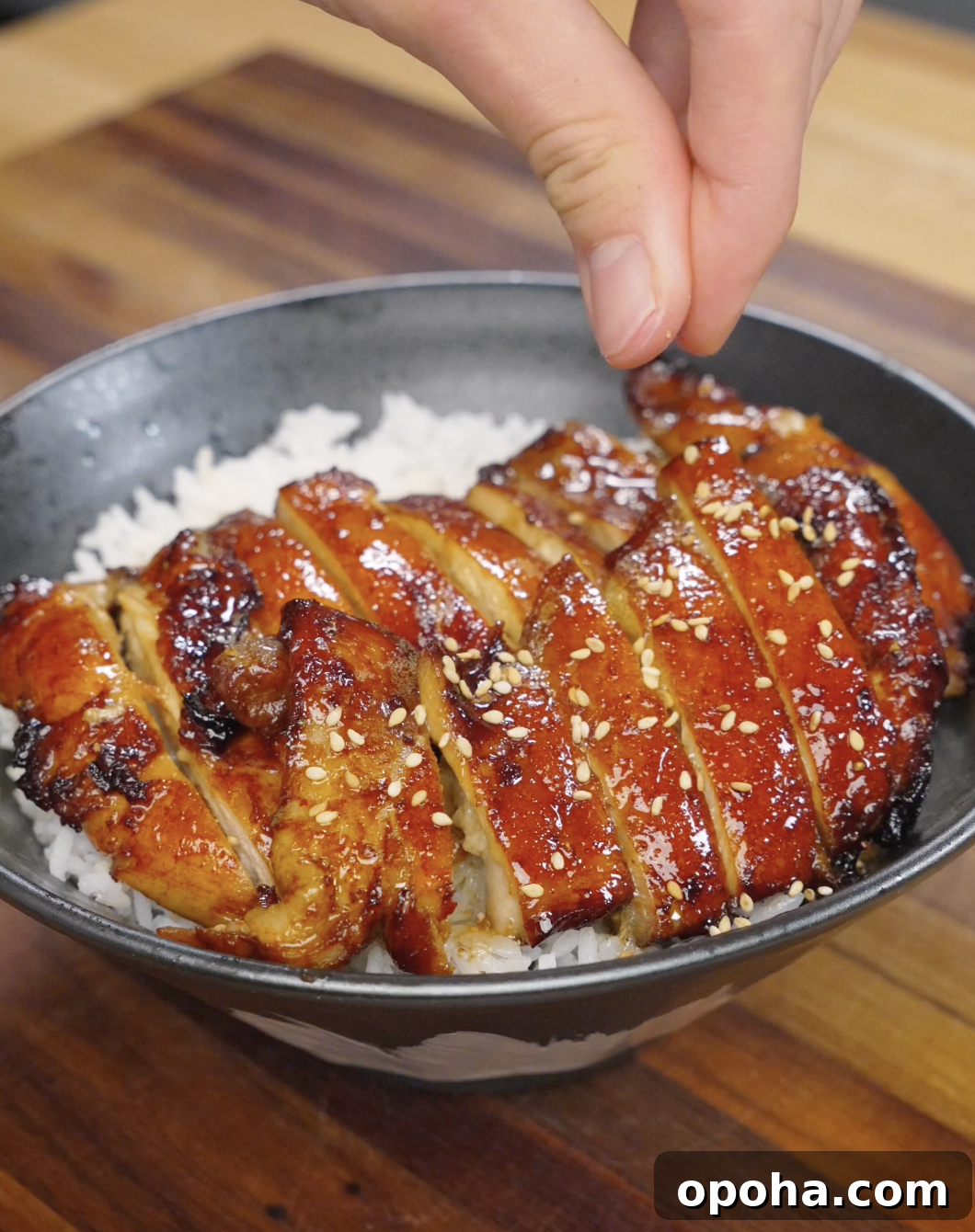 Sesame seeds being sprinkled over sliced chicken bulgogi on top of rice, adding texture and nutty flavor to the finished dish.
