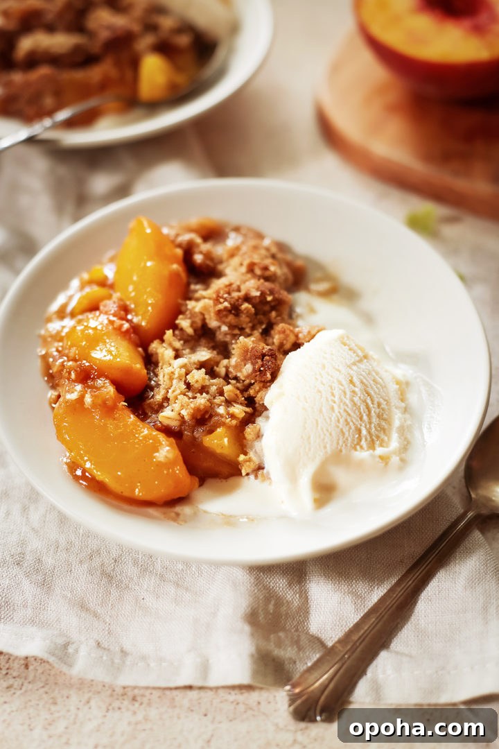 close up of peach oat crisp on a white plate with a scoop of vanilla ice cream