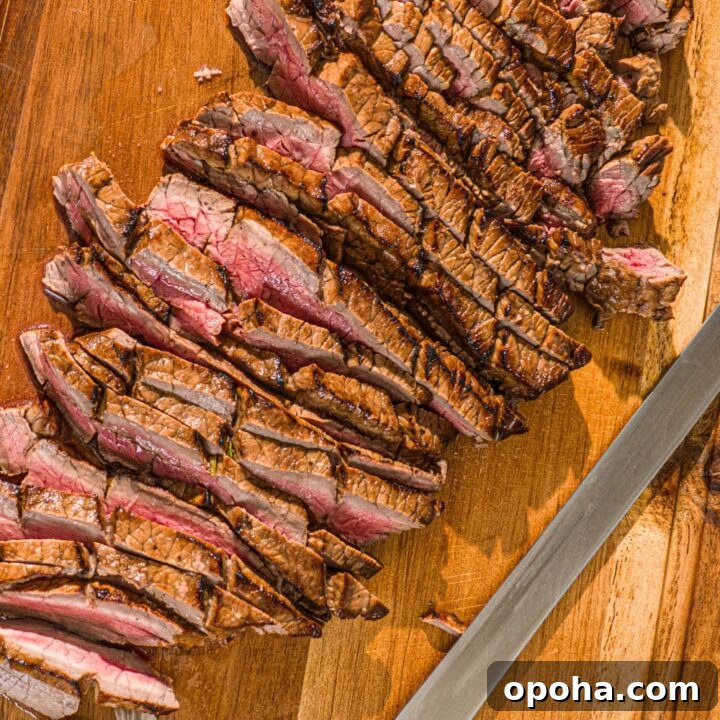 A london broil sliced into a bunch of thin slices on a wooden cutting board.