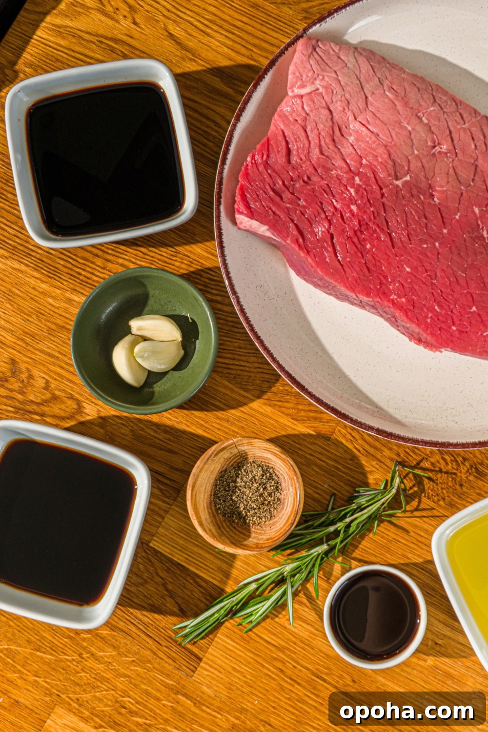 Bowls containing ingredients to make London broil marinade including London broil beef, soy sauce, balsamic vinegar, Worcestershire sauce, garlic, rosemary, and black pepper.