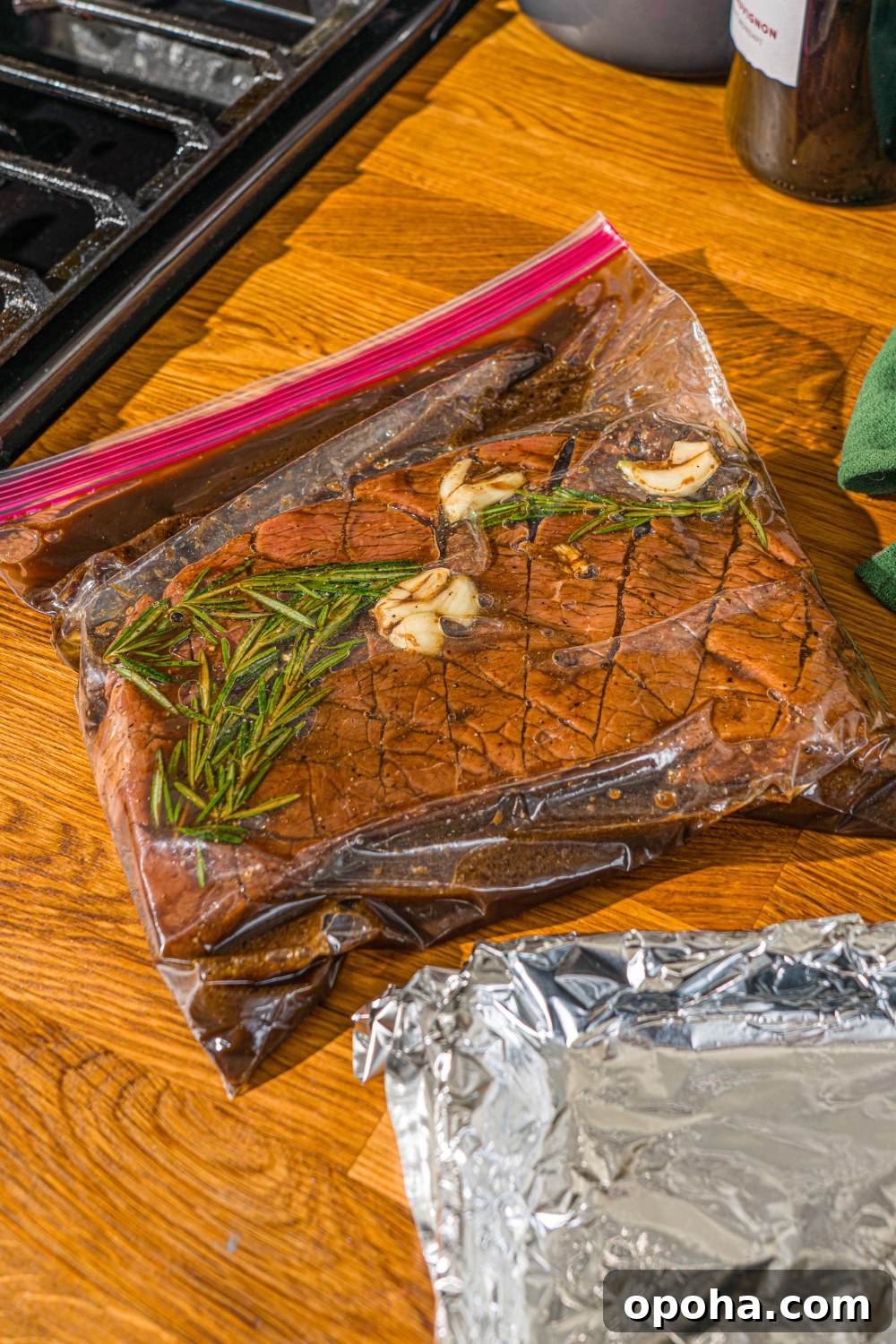 London broil beef in a resealable bag marinating in marinade on a wooden counter.