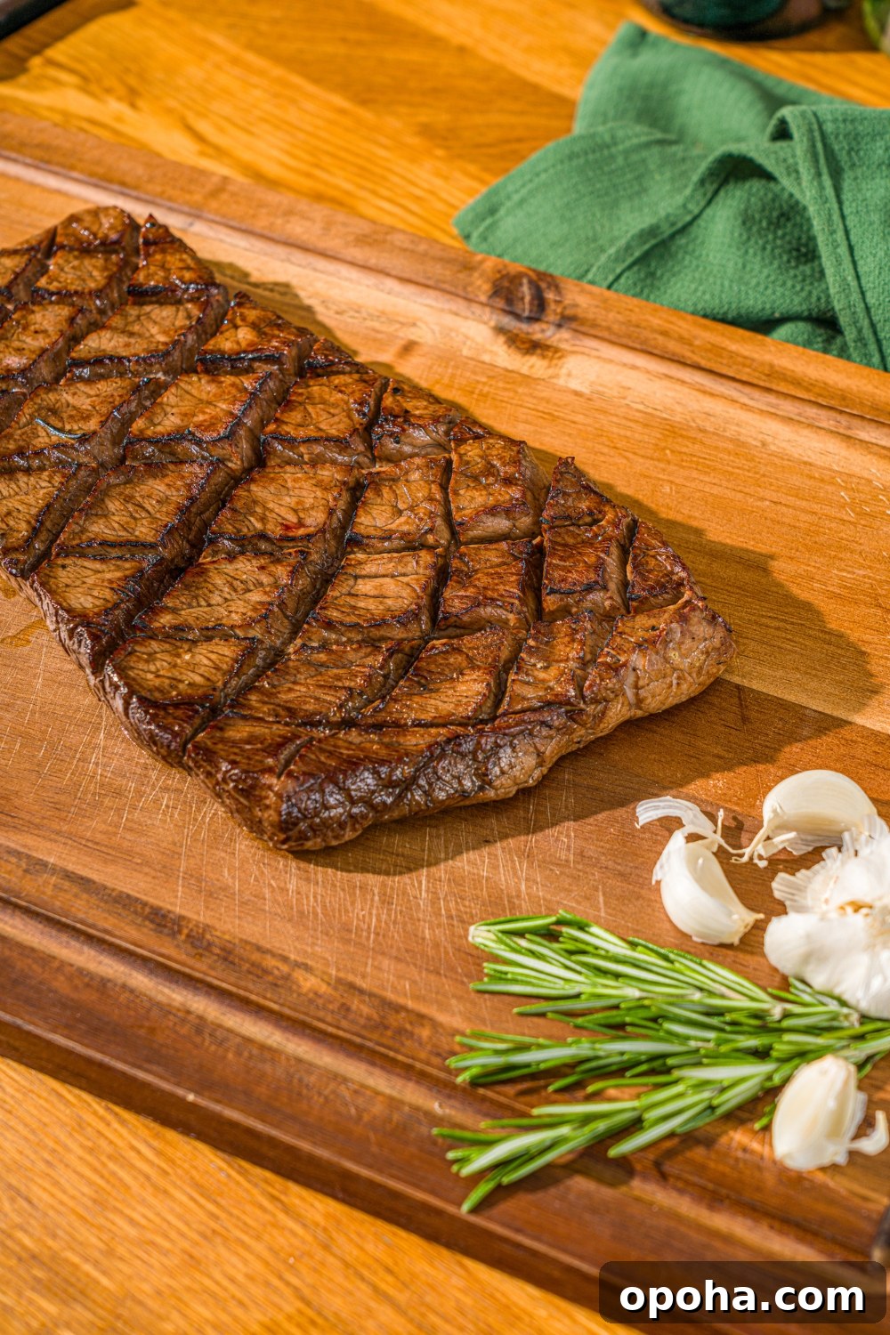A marinated and grilled London broil on a wooden cutting board served with garlic and rosemary.