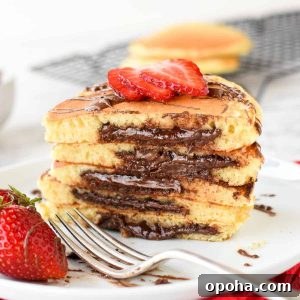 Fluffy Nutella-Stuffed Pancakes 8 five stacked nutella filled pancakes on white plate sliced in half showing the nutella oozing out